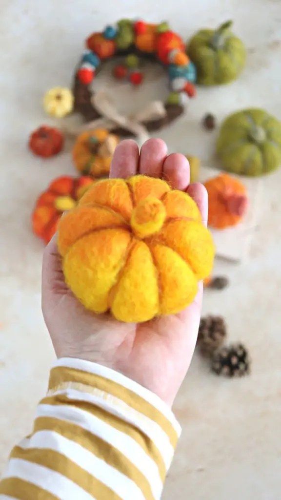 A bright orange DIY pumpkin held in the palm of the hand for size reference. Caption says: easiest ever needle felting project