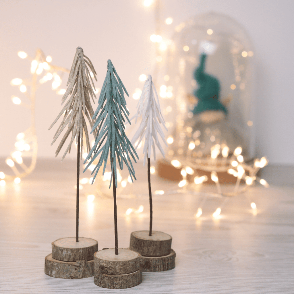 Image shows felt christmas trees . In the background is a Christmas nome lit with pretty fairy lights