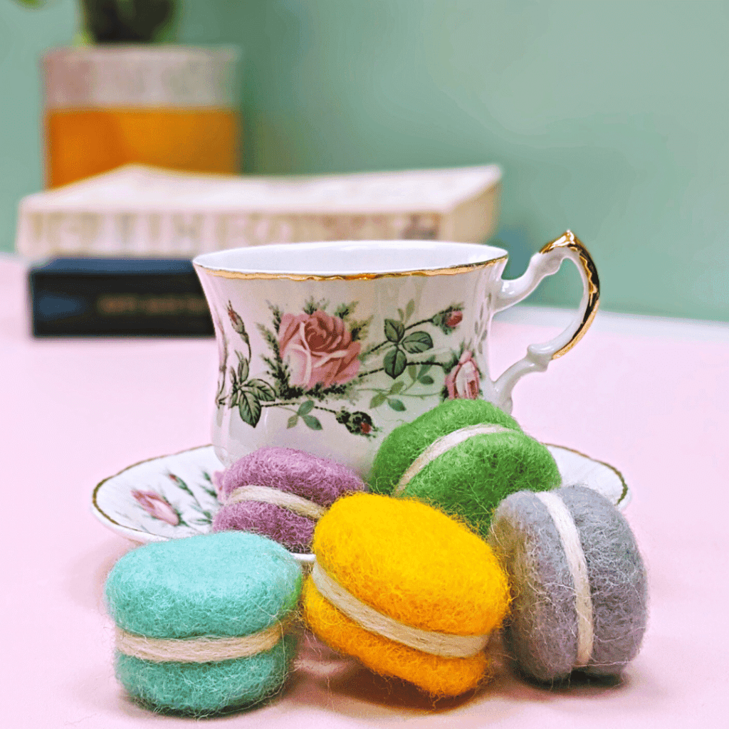 image shows realistic needle felted cakes next to a pretty china tea cup and saucer